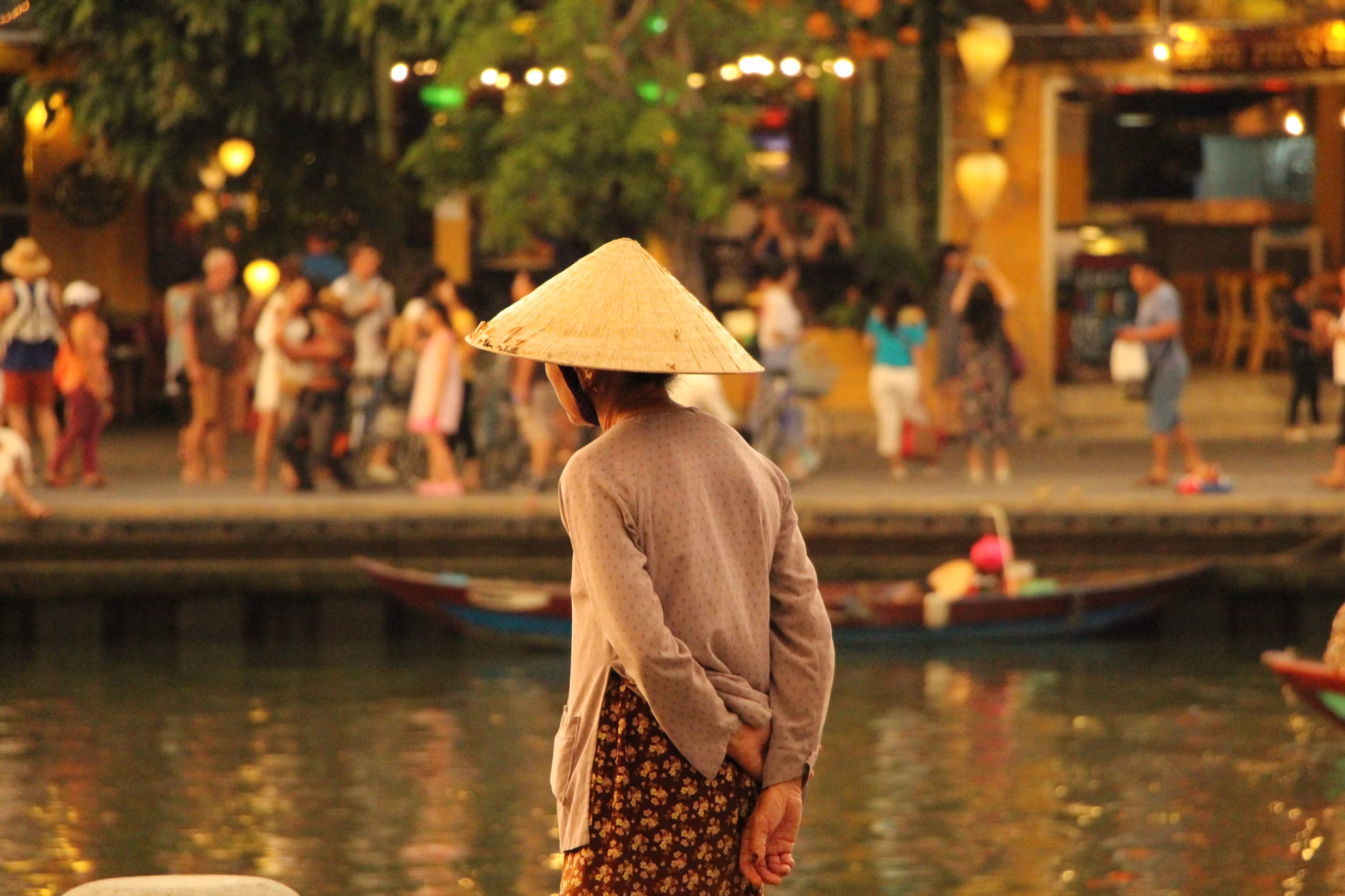 A woman in a conical hat by the river at dusk